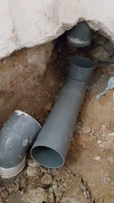 Reparación de red de saneamiento enterrada con tubo y codos de PVC.